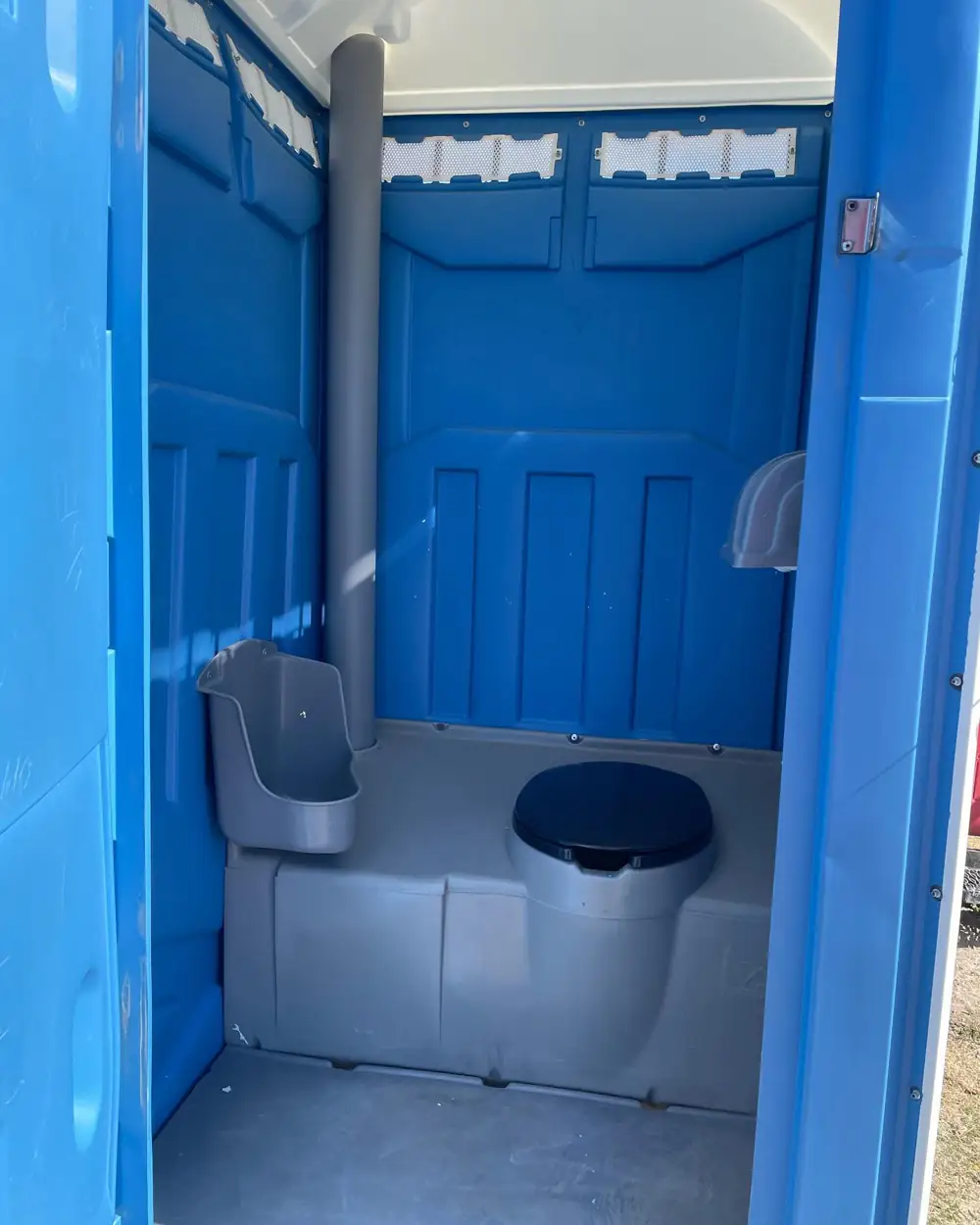 Inside a cleaned standard porta potty with urinal, seat and paper holders